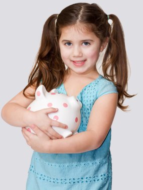 Cute little girl cradles a pink polka dotted piggybank in arms. clipart