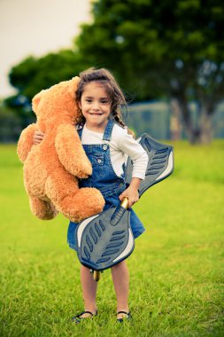 Cute girl standing in the grass holding teddy bear clipart