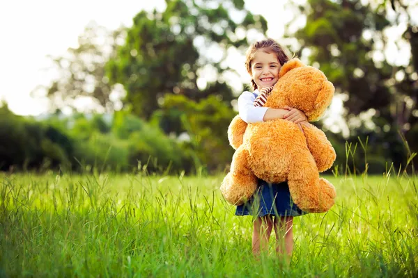Małe słodkie dziewczyny stojąc w trawie trzyma misia — Zdjęcie stockowe