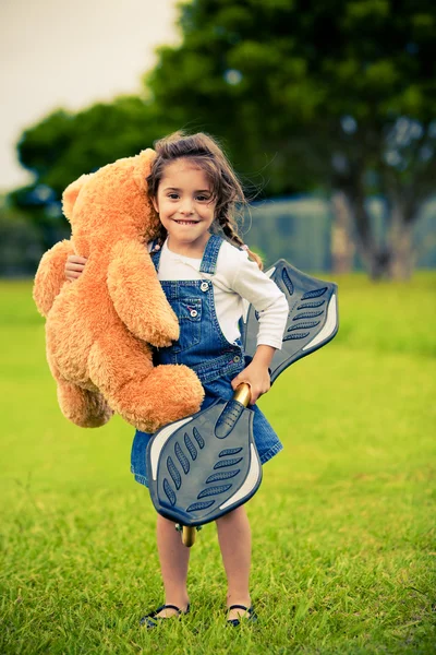 テディー ・ ベアを保持している草の中に立っているかわいい女の子 — ストック写真