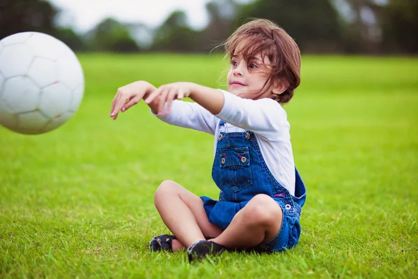 ボールを投げる草の上に座っている若い女の子 — ストック写真