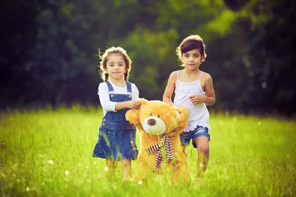 Dwie dziewczynki w trawie z misiem — Zdjęcie stockowe