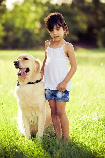 Chica de pie en la hierba con golden retriever — Foto de Stock