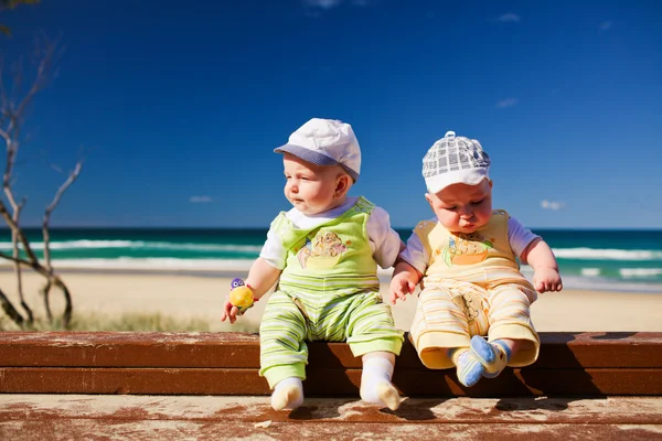 Dois gêmeos gêmeos bebê irmão sentado em um molhe de praia — Fotografia de Stock
