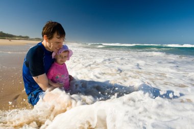 Dad and baby daugher setting on the beach clipart