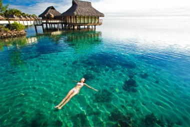 Young woman in white bikini swimming in a coral lagoon clipart