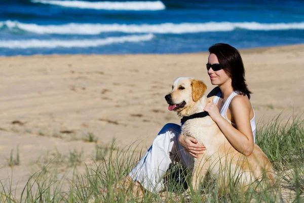 坐着一条狗的海滩上的年轻女性 — 图库照片