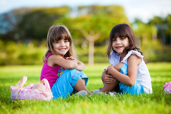 Twee jonge meisjes in het gras zitten glimlachen — Stockfoto