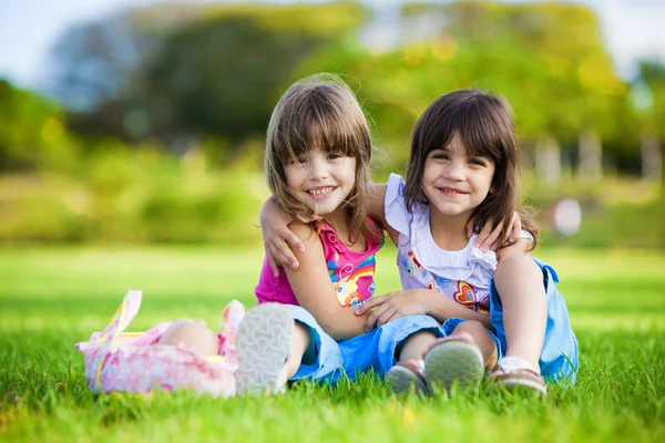 Две юные улыбающиеся девушки обнимаются в траве — стоковое фото