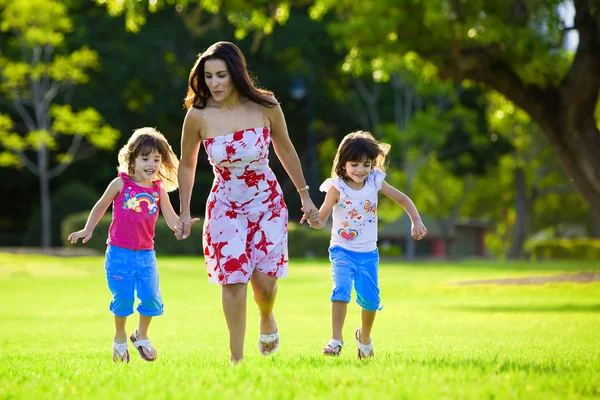 Opgewonden moeder en twee dochters springen in gras — Stockfoto