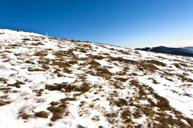 Mountain scenery out of the grass under the snow in the foreground clipart