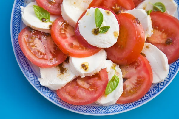 Insalata Caprese in blue and white plate on bright blue background; — Stock Photo, Image