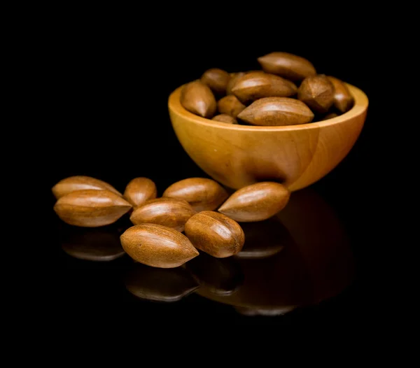 Pecan nuts in small wooden bowl and scattered; isolated; on black mirror, — Stock Photo, Image