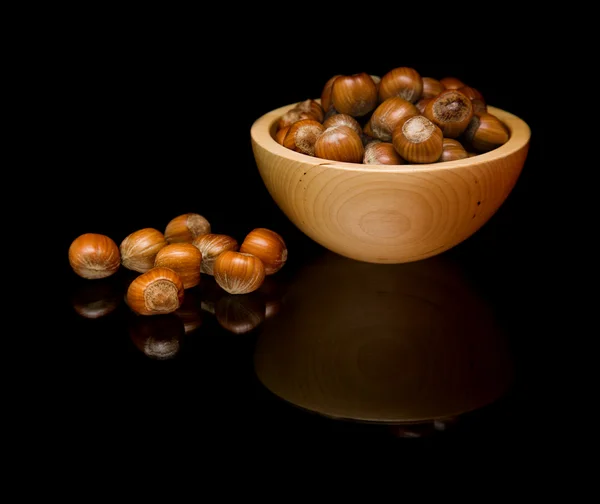 Lískové ořechy v malé dřevěné misky a rozptýlené; izolovaná; na černé zrcadlo — Stock fotografie