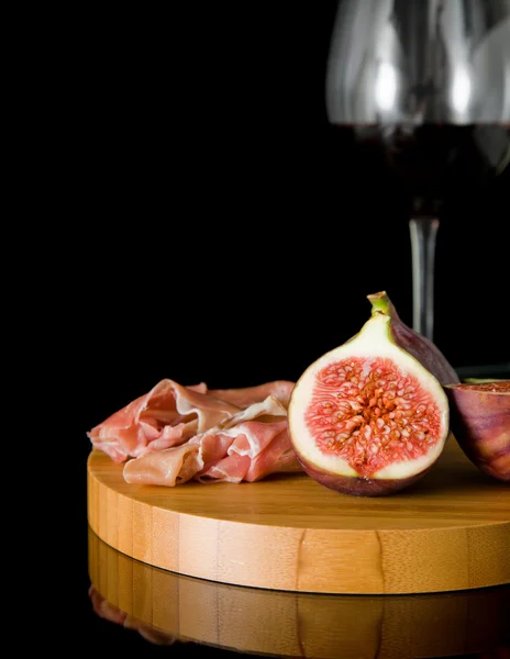 Свежий инжир; Прошутто и красное вино на небольшой круглой доске, на черном — стоковое фото
