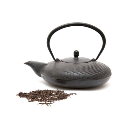 Cast iron eastern black teapot and scattered dry tea leaves on white background clipart