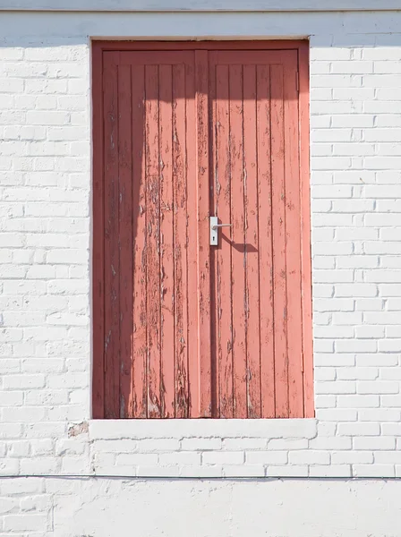 Pink door in white brick wall, high above the ground