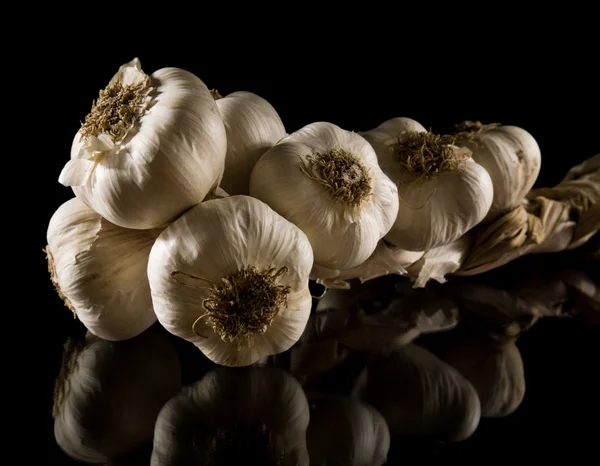 Plait of garlic bulbs close-up isolated on black background with reflection — Stock Photo, Image