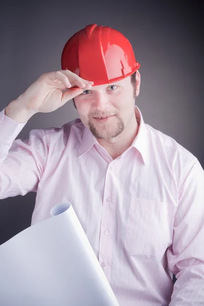 Młody inżynier z plany podnosi jego kapelusz — Zdjęcie stockowe