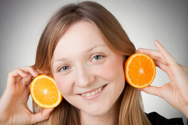 Beautiful blond girl using orange as earrings — Stock Photo, Image