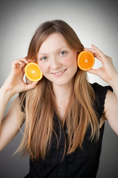 Beautiful blond girl using orange as glasses, with grey backgrou — Stock Photo, Image
