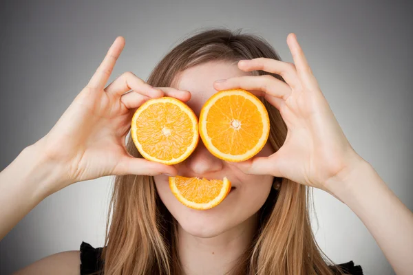 stock image Beautiful blond girl using orange as glasses, with grey backgrou