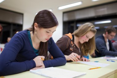 pretty female college student sitting an exam in a classroom full of students (shallow DOF; color toned image) clipart