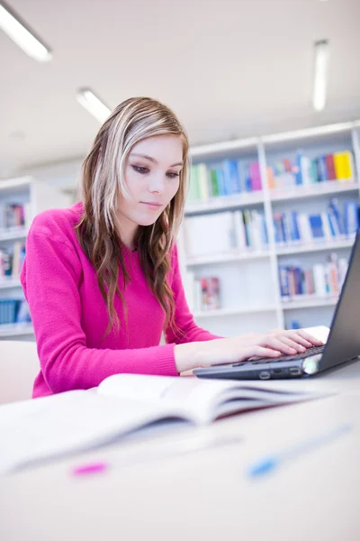 В библиотеке - симпатичная студентка с ноутбуком и книгами. — стоковое фото