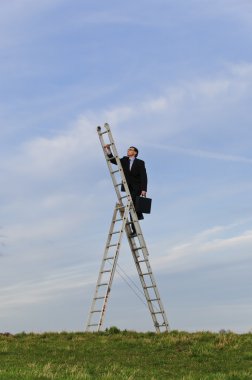 Businessman, manager in a dark suit stands in the middle of a meadow on the career ladder and looks into the landscape with clouds of heaven. clipart