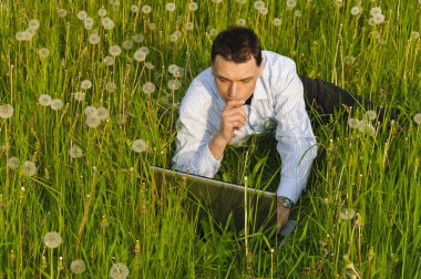 Businessman in suit standing on a meadow and looks into the distance in front of clouds clipart