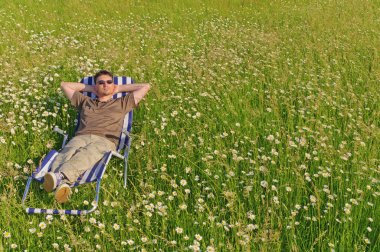 Man in meadow relaxing in deck-chair clipart