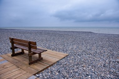 Wooden bench at a pebbles beach clipart