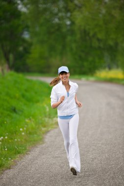 Koşu - sportif bir kadın yolda koşuyor, kulaklıkla müzik dinliyor.