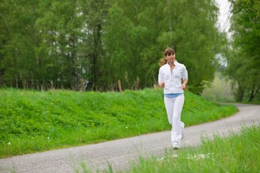 Koşu - sportif bir kadın yolda koşuyor, kulaklıkla müzik dinliyor.