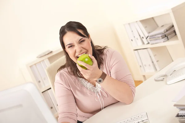 年轻女商人咬苹果在现代办公 — 图库照片