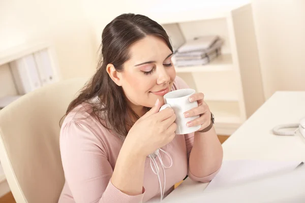 在办公室坐在桌前吃喝咖啡休息的快乐女商人 — 图库照片