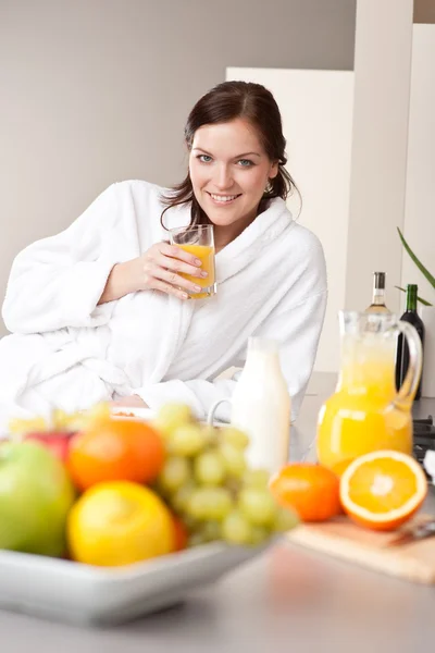 Νεαρή γυναίκα ποτό χυμό πορτοκάλι για πρωινό στην κουζίνα — Φωτογραφία Αρχείου