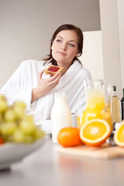 年轻女子穿浴袍在厨房里吃早餐吃吐司 — 图库照片