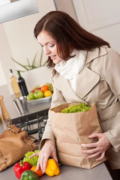 Jovem mulher desembalagem saco de compras na cozinha — Fotografia de Stock