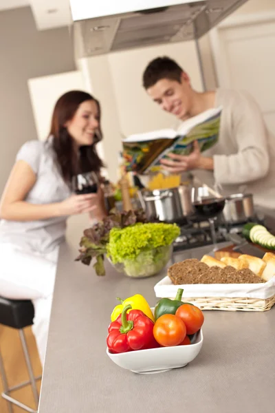 レシピ料理を飲む赤ワインを選ぶのキッチンで若いカップル — ストック写真