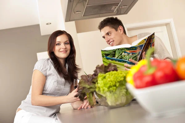 Jovem casal na cozinha escolhendo receita do livro de receitas — Fotografia de Stock