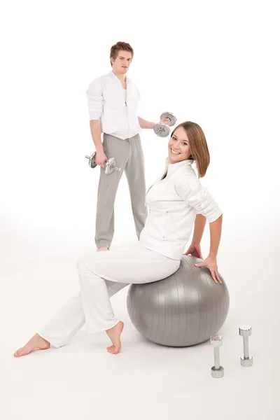 Casal jovem com pesos e bola de fitness em branco — Fotografia de Stock
