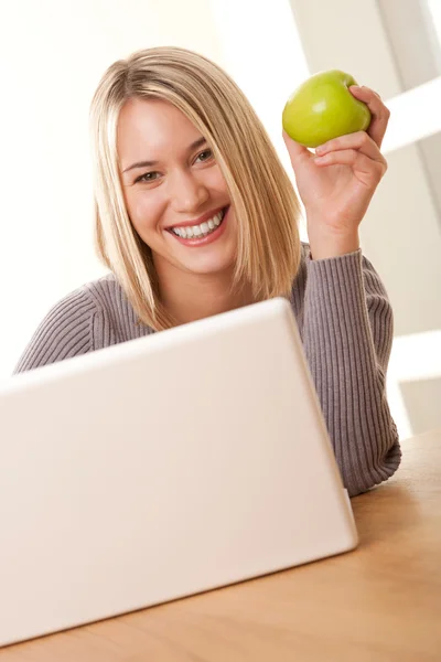笑顔金髪の学生のノート パソコンと食用リンゴの操作 — ストック写真