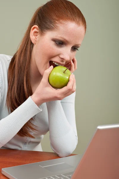 Μακριά κόκκινα μαλλιά γυναίκα δάγκωμα μήλο στο γραφείο — Φωτογραφία Αρχείου