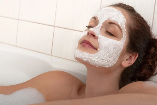 浴槽の中で横になっている顔のマスクを持つ若い女 — ストック写真