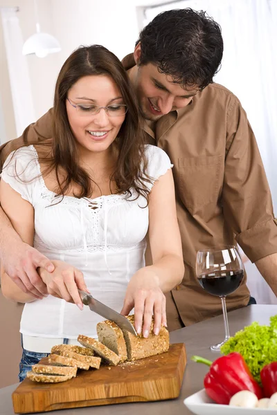 幸せなカップル一緒に近代的なキッチンでパンをカットし 赤ワインを飲む — ストック写真