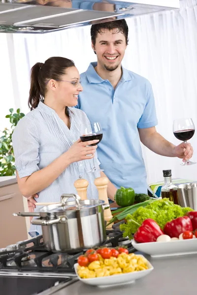 微笑着对夫妇喝红酒与蔬菜的厨房里做饭 — 图库照片