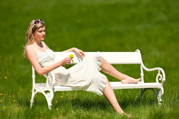 Spring - Young woman relaxing on bench in meadow — Stock Photo, Image