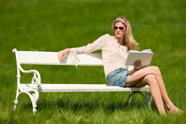 年轻的金发美女坐在白色长椅上用书 浅景深 — 图库照片