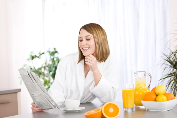 Café da manhã - Mulher sorridente lendo jornal na cozinha — Fotografia de Stock